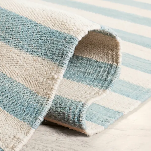Newport Azure Stripe Wool Flatweave — Binding Detail Rolled wool flatweave rug showing hand-stitched bound edge and blue-ivory stripe pattern