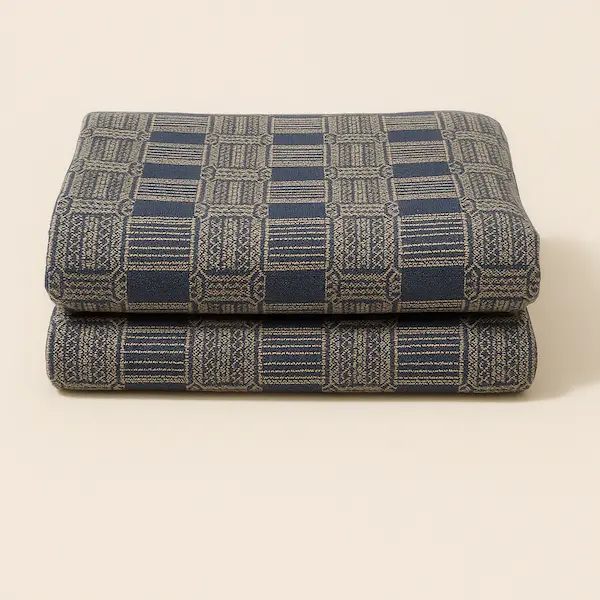 Folded Highland Manor Jacquard throw in navy and beige, featuring a four-side hem and intricate woven geometric pattern, displayed on a neutral beige background.