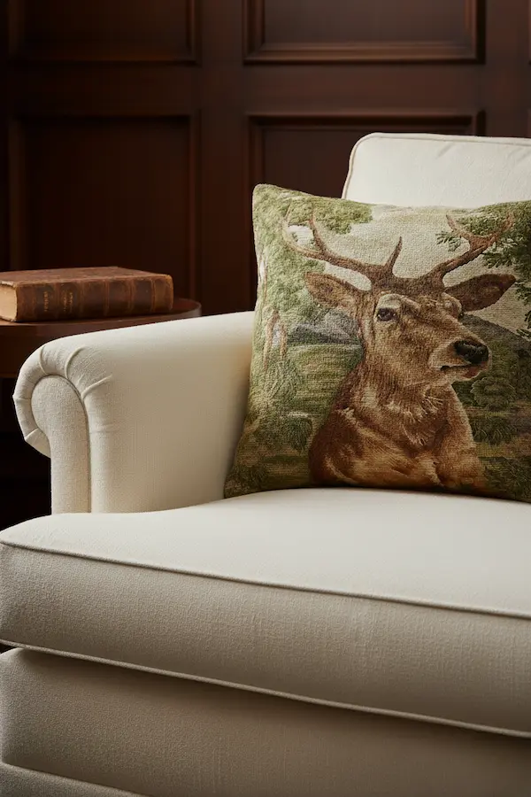 * Noble Stag Tapestry Pillow – Rustic Woodland Cushion in Interior Setting Noble Stag Tapestry Pillow styled on a cream armchair, handmade jacquard cushion with stag motif and velvet back