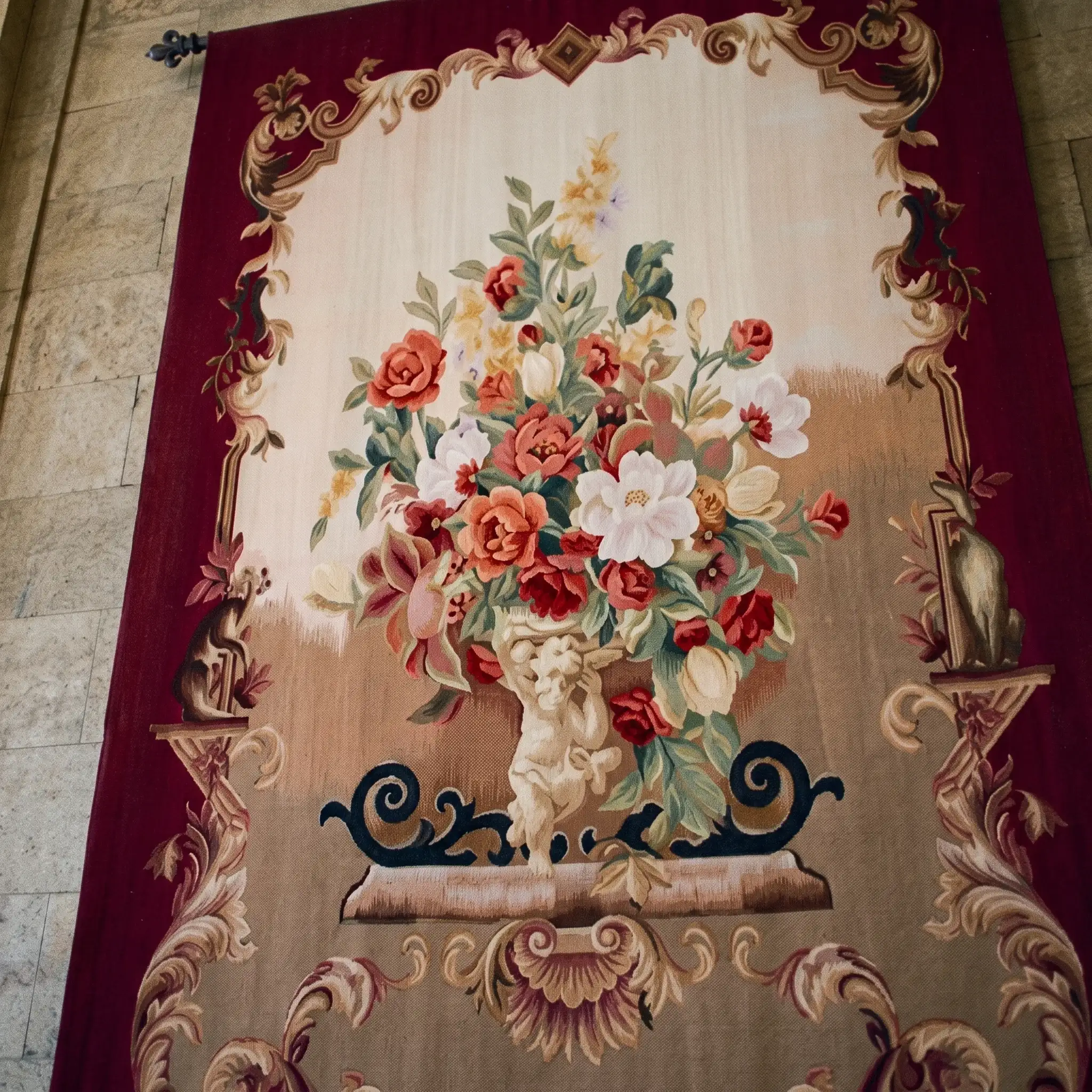 Burgundy Rose Urn Wall Tapestry 4 Burgundy Rose Urn wall tapestry hanging from a fleur-de-lys rod against a pale stone wall
