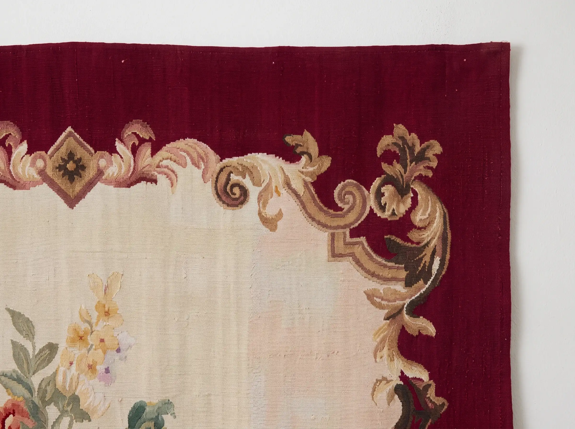 Burgundy Rose Urn Wall Tapestry 3 Corner of a handwoven wool tapestry showing gold and cream acanthus scrolls on a burgundy border around a cream ground