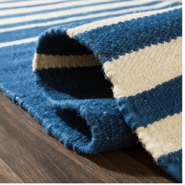 Montauk Regatta Stripe Wool Flatweave — Rolled Binding Detail Rolled wool flatweave rug showing hand-stitched binding and underside of navy-and-ivory stripes on dark wood