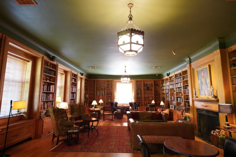 Dark academia style home library with rich wooden bookshelves, leather seating, and warm ambient lighting