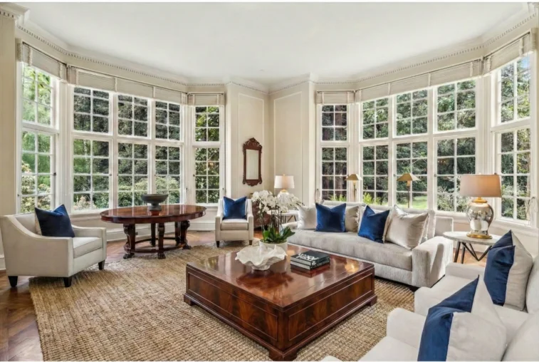 Expansive Woodside estate great room featuring floor-to-ceiling windows, a substantial mahogany coffee table, and natural fiber rugs designed for indoor-outdoor California living.