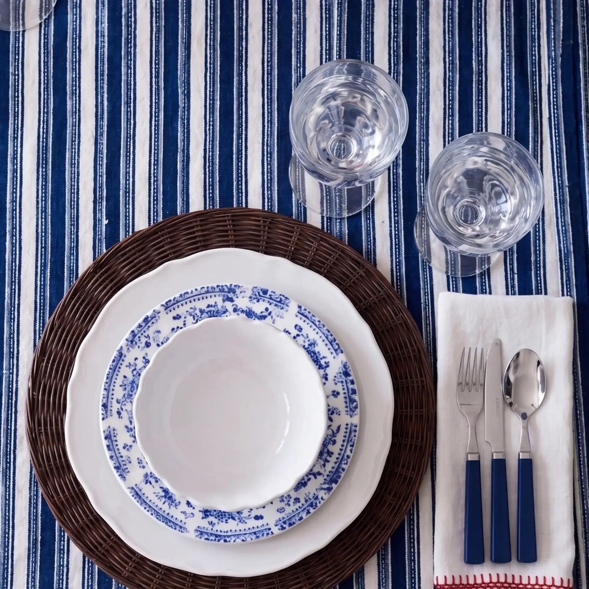 Montecito Round Rattan Placemat 3 Montecito Round Rattan Placemat styled with blue and white dinnerware, glassware, and striped table linen