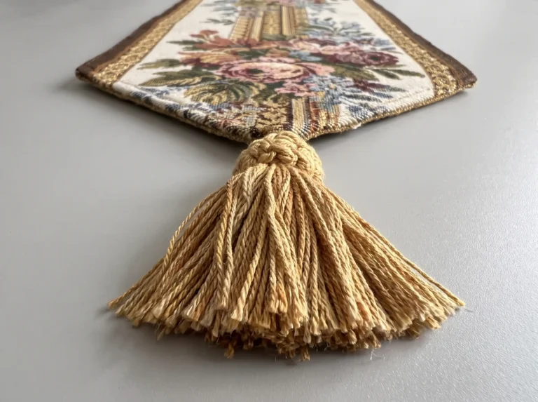 Close-up of the hand-tied gold cotton tassel at the pointed end of a floral jacquard table runner
