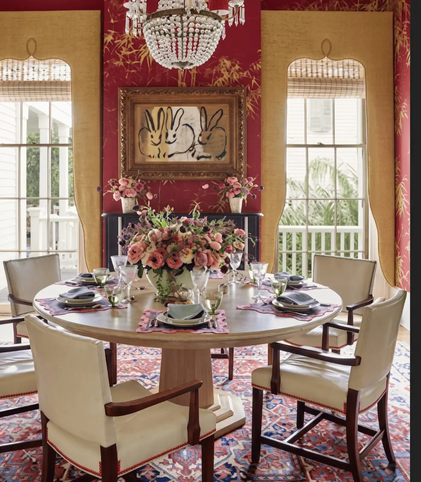 Red and gold dining room with crystal chandelier, Persian rug, Hunt Slonem rabbit painting — repetition as the organizing principle